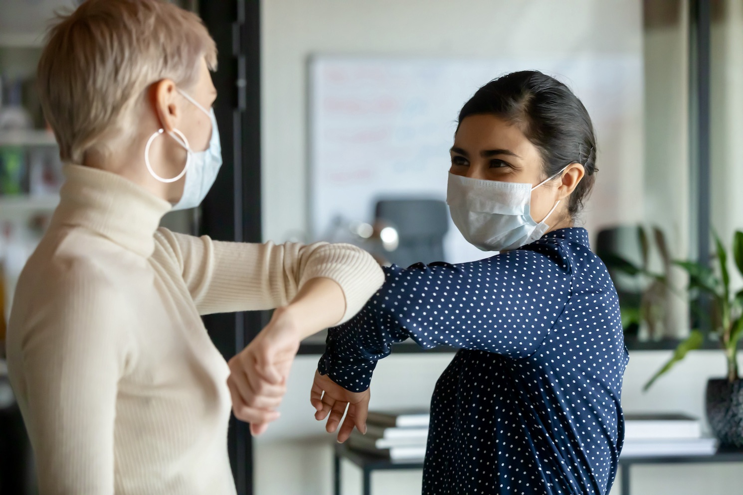 Smiling,diverse,female,colleagues,wearing,protective,face,masks,greeting,bumping